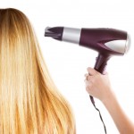 Woman with long blond hair and stylist with hairdryer at hairdressers